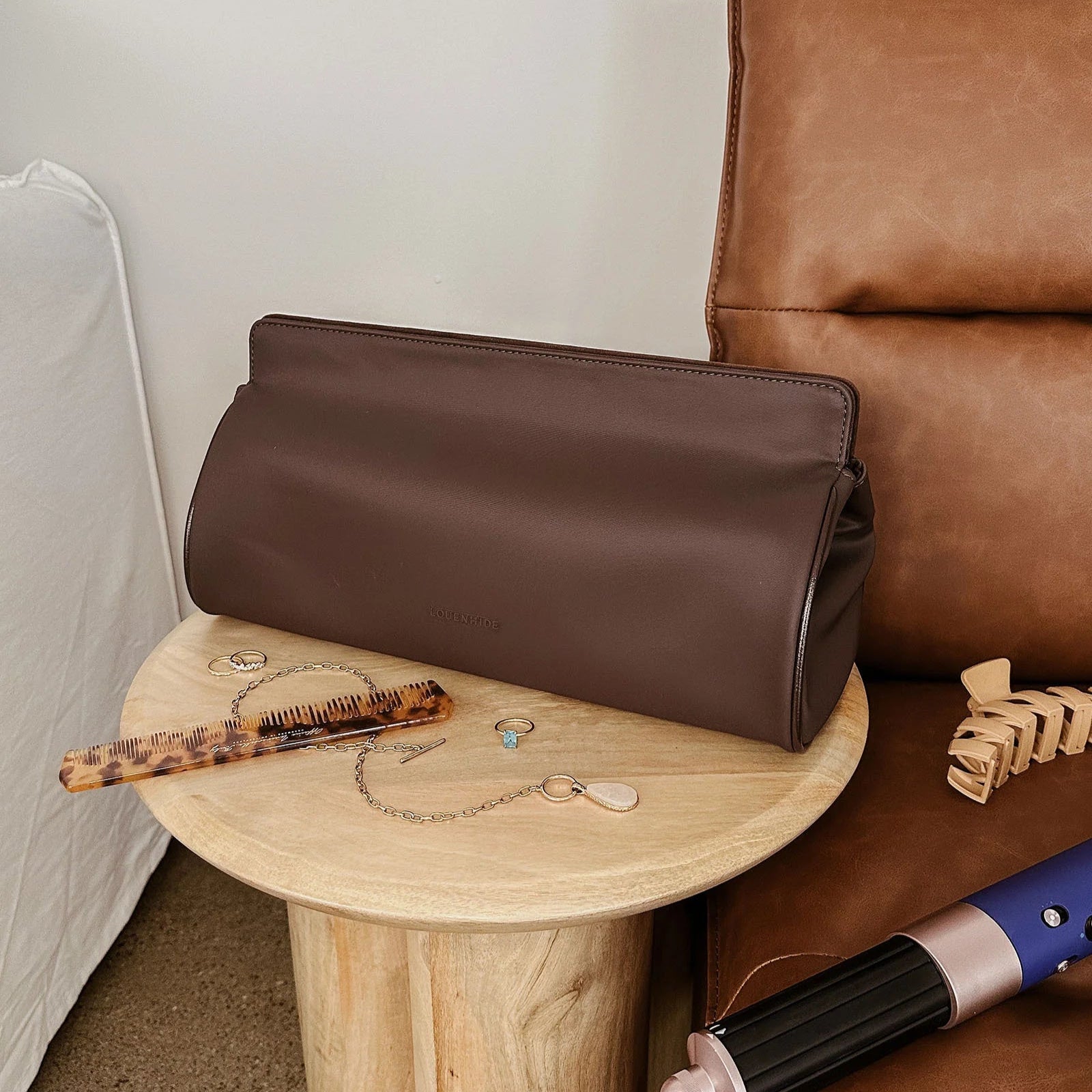 Brown leather bag on a wooden side table next to a brown leather couch.